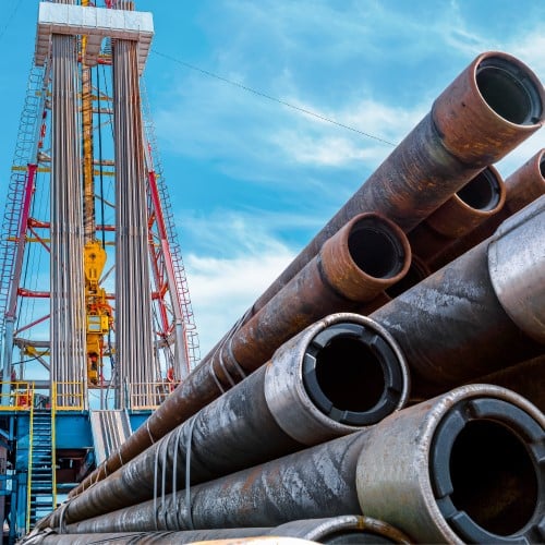 Empty pipes piled in front of a drilling rig