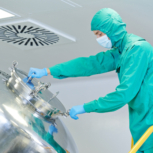 Pharmaceutical worker wearing PE opening a stainless steel tank